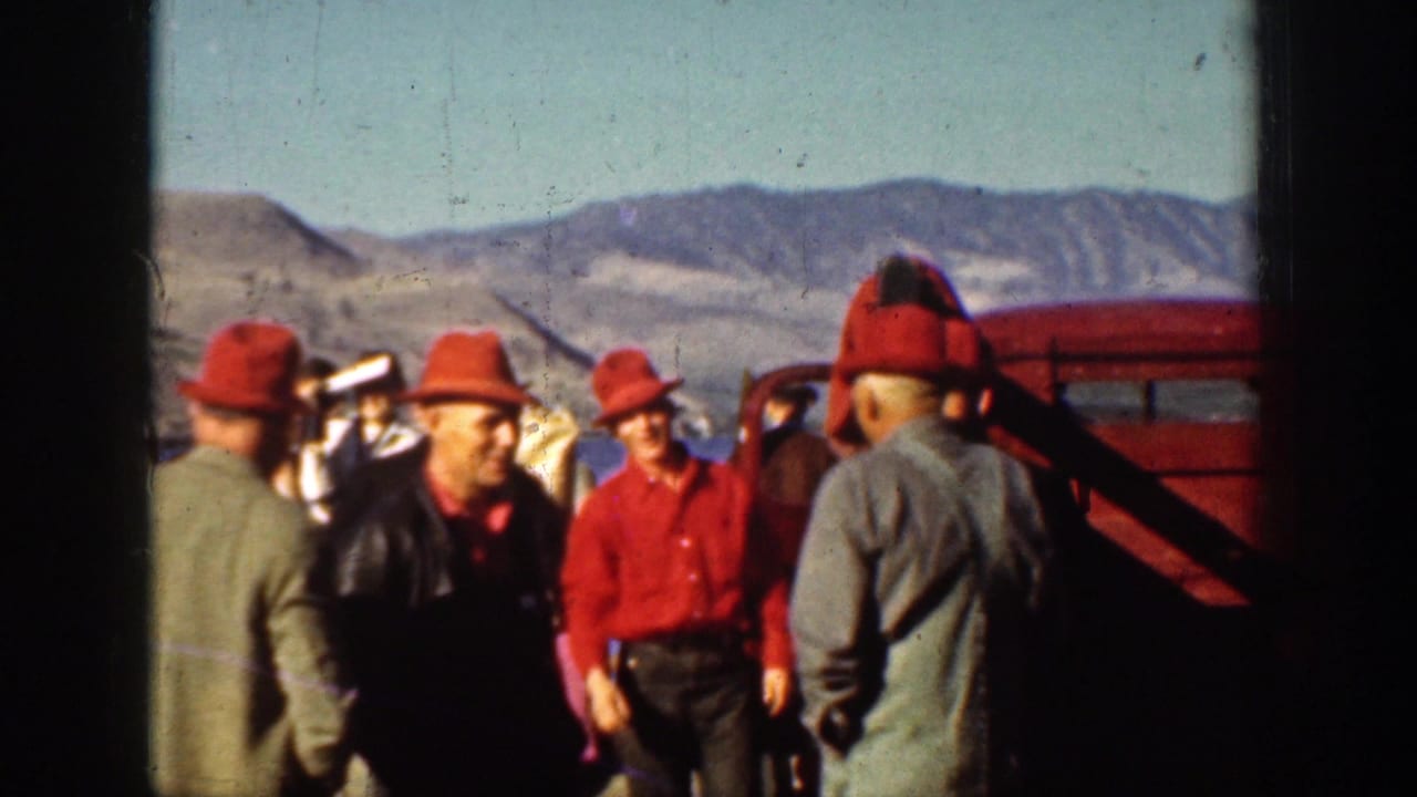 Men in red hats gathered near a red vehicle with dry mountains behind them.