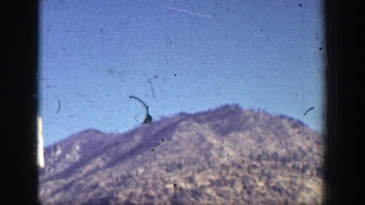 A dry brown mountain ridge near Chelan fills the frame beneath a bright blue sky in soft 8mm color.