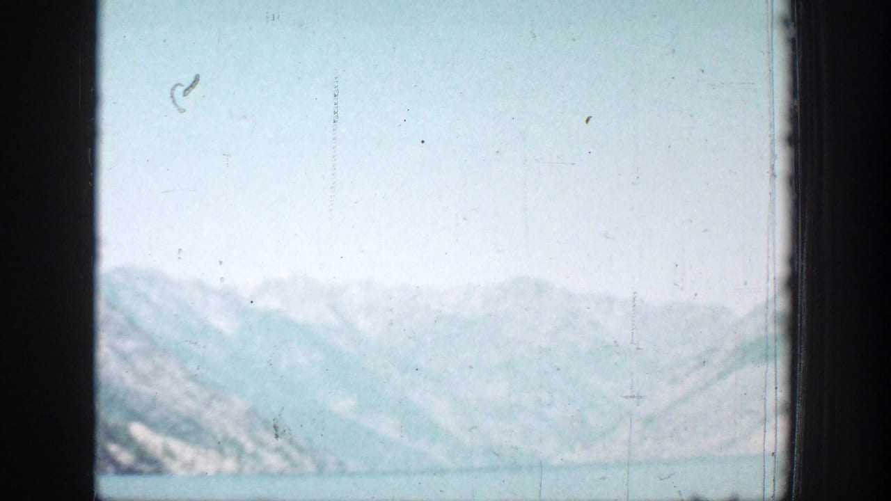 Distant mountains across Lake Chelan under a pale sky, with faded color and visible film wear from the 8mm scan.