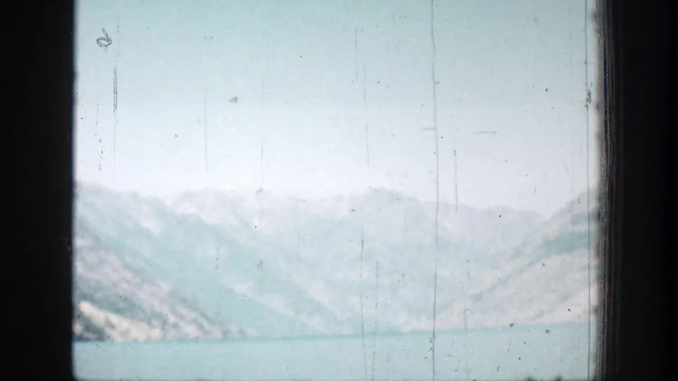 Soft 1939 8mm view of a calm lake and pale mountain ridges in the Chelan, Washington area, partly framed by dark vehicle or window edges.