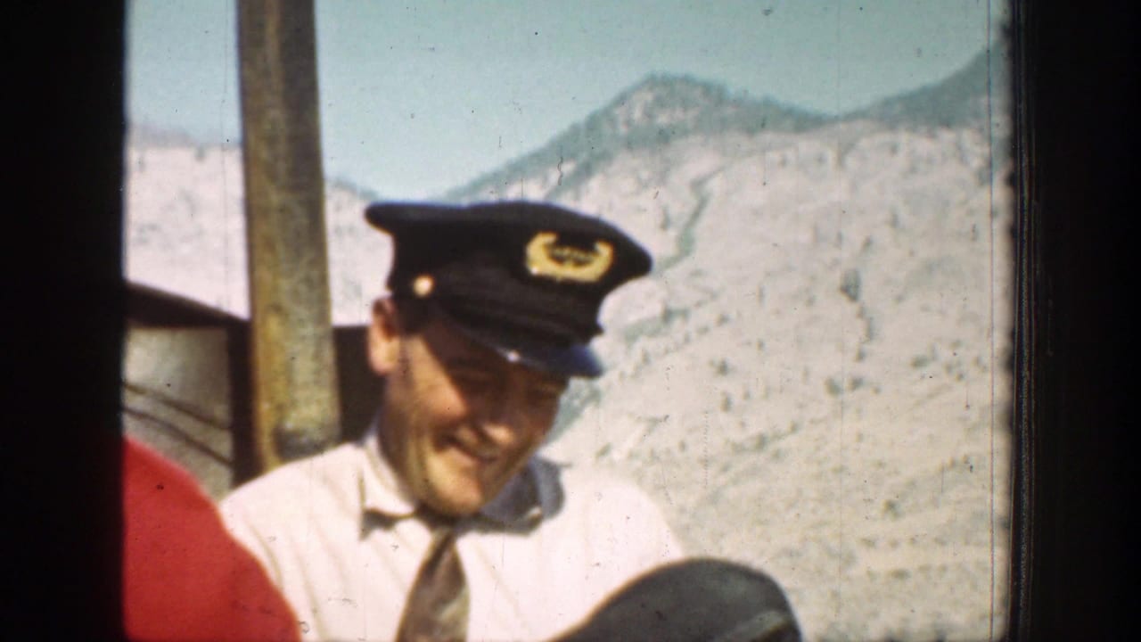 Smiling man in a pilot-style cap beside mountain scenery.