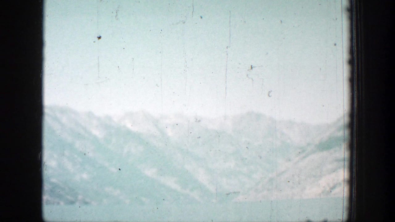Hazy 8mm view of Lake Chelan-area water and snow-dusted mountain ridges, with scratches and soft exposure visible across the frame.
