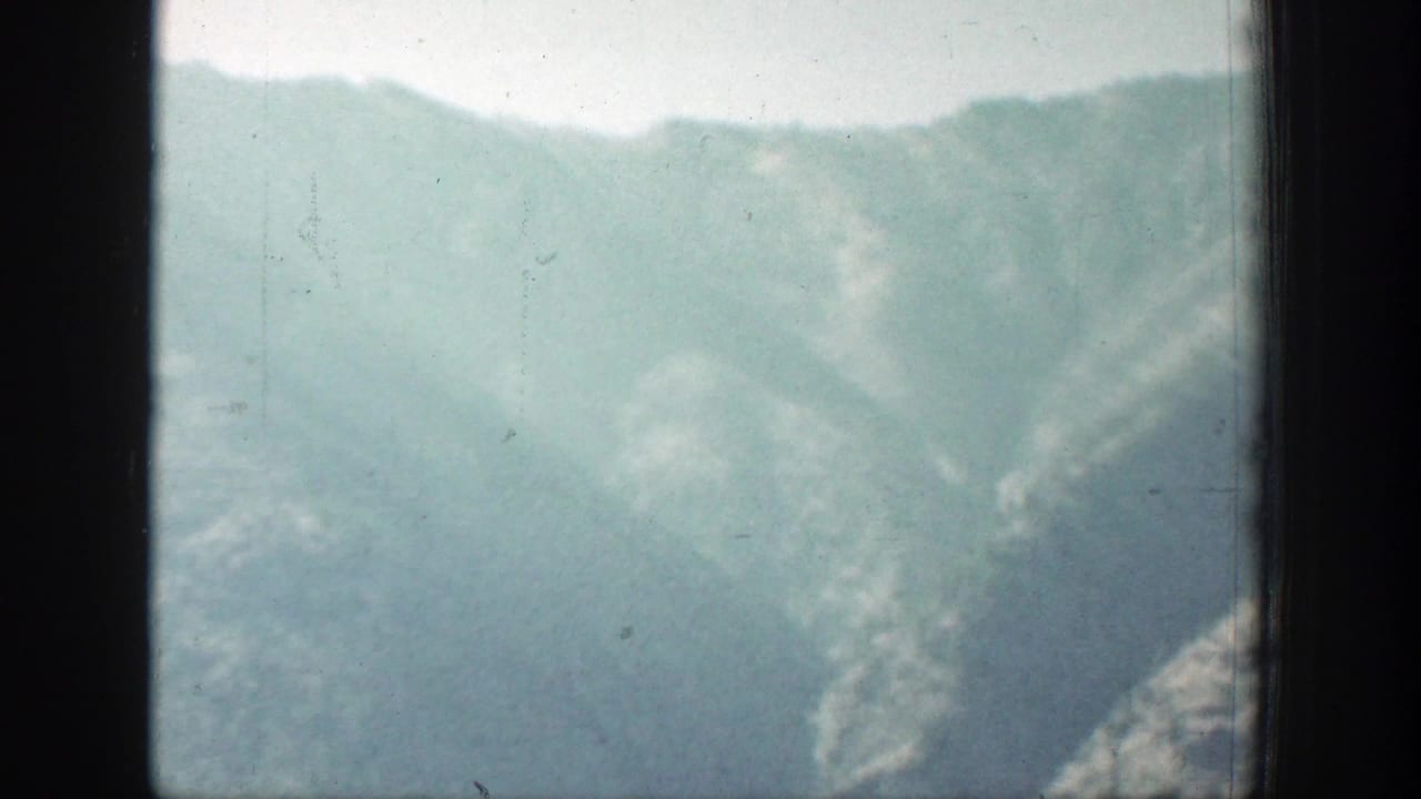 A blurred Chelan-area mountain slope fills the frame, with pale sky, dark side framing, and visible 8mm dust and scratches.
