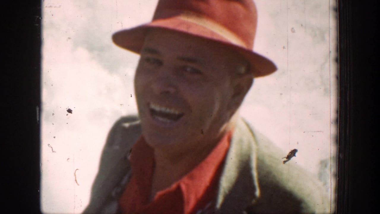 Smiling man in a red hat seen from inside a vehicle.