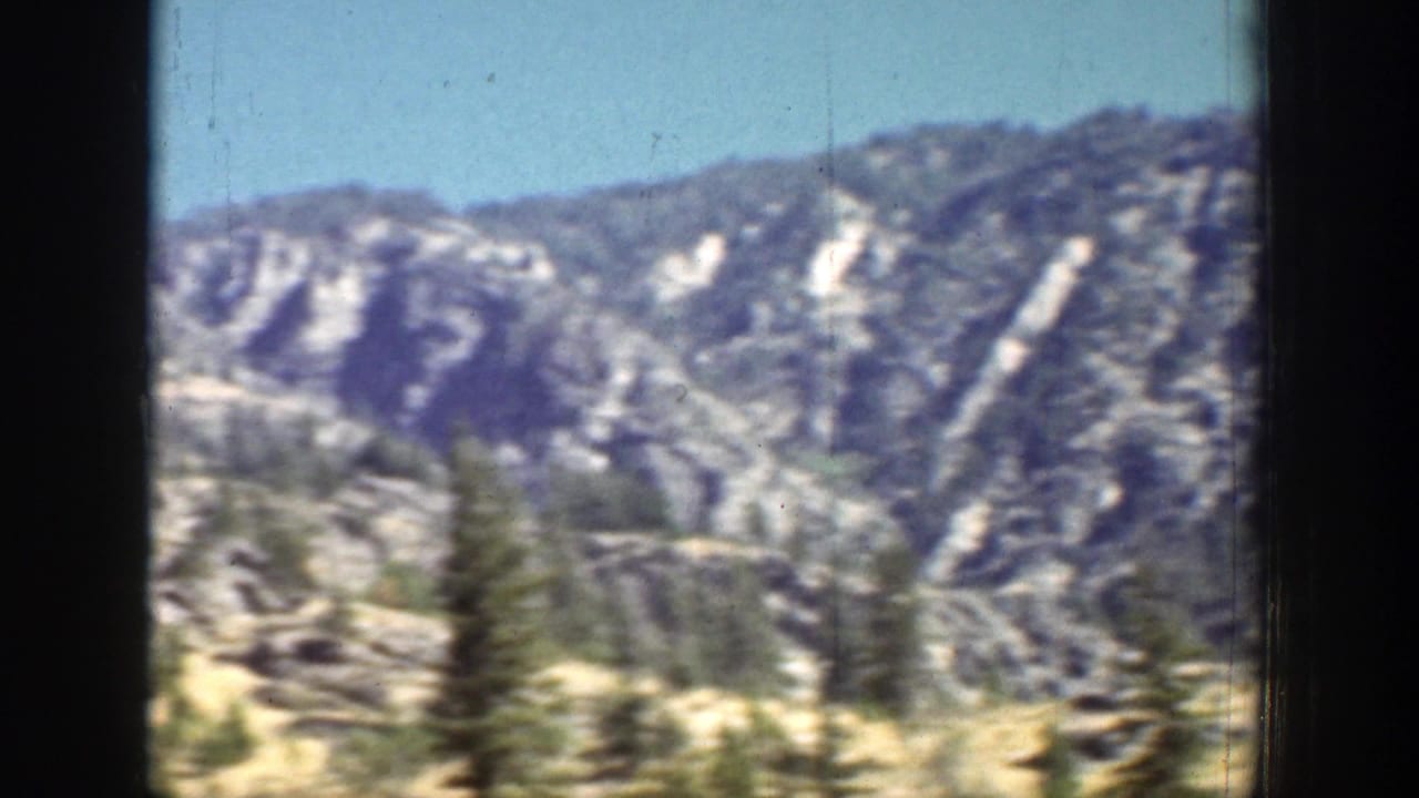 Mountain terrain near Chelan appears beyond blurred roadside evergreens in this 1939 home-movie frame.