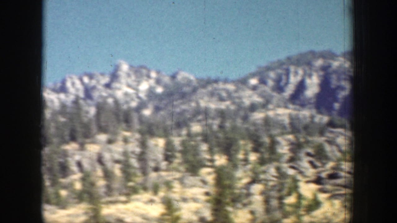 Chelan-area mountain ridges and evergreen forest are seen from a moving vehicle in 1939 8mm footage.