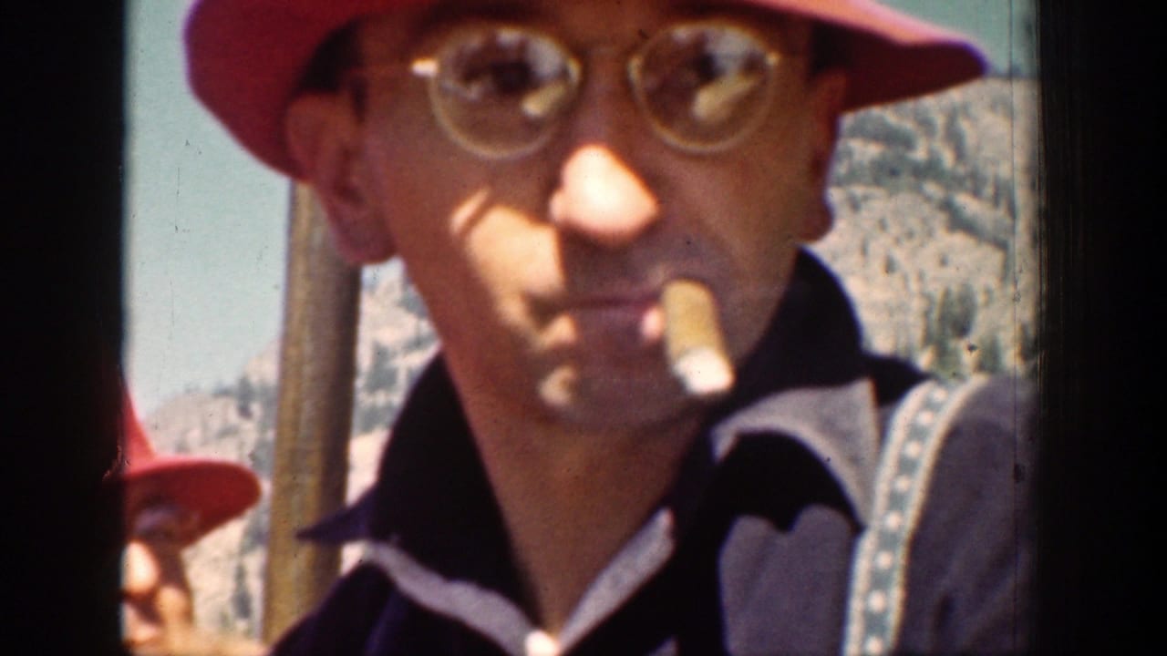 In this 1939 Chelan, Washington home-movie frame, a man in a red hat and eyeglasses smokes beside a framed mountain view.