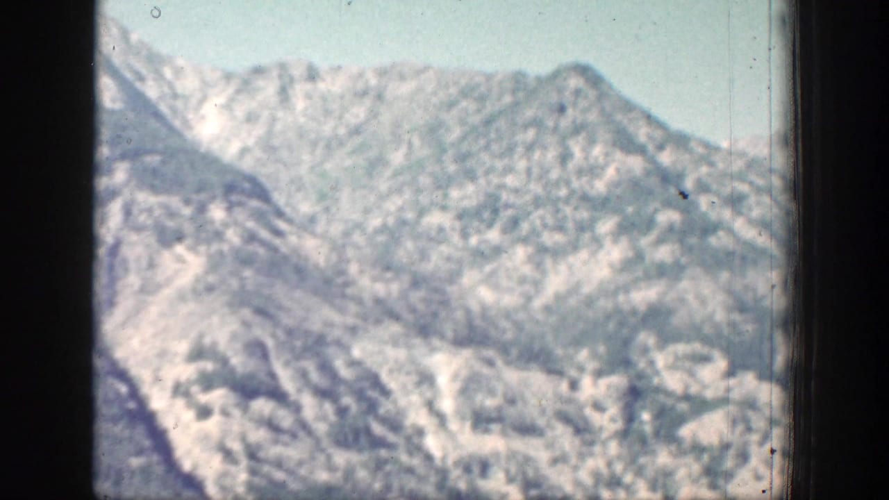 1939 Chelan-area 8mm frame of a distant snow-dusted mountain ridge seen through soft film grain.