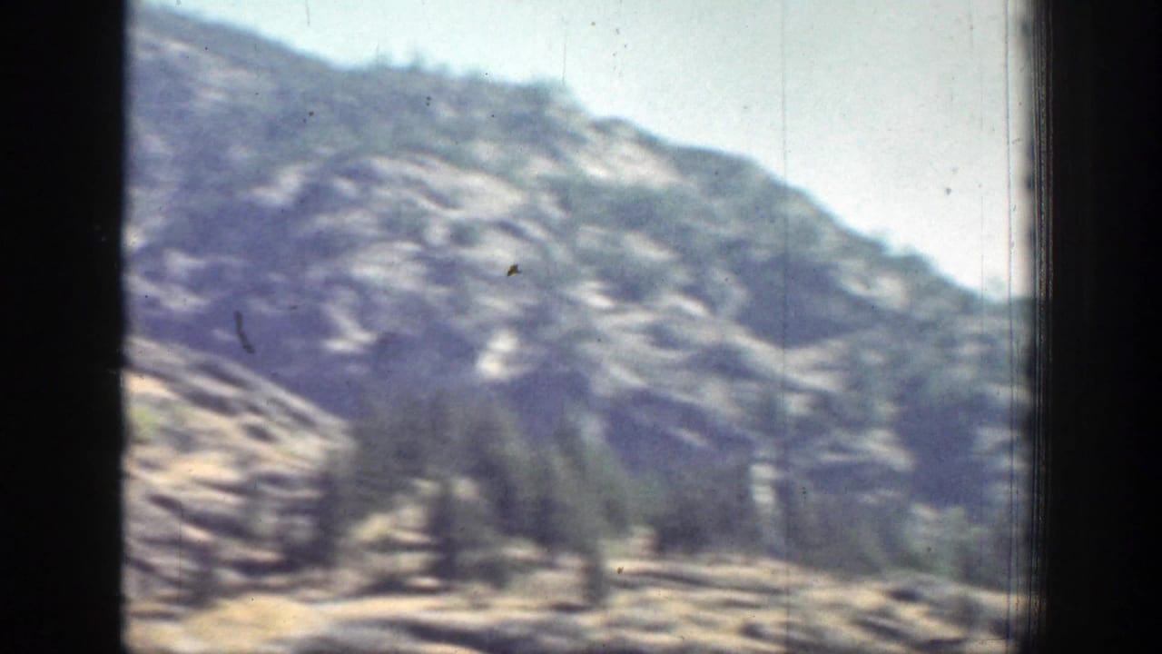 Faded 8mm view of a Chelan-area mountainside with layered rock, sparse trees, and pale open ground.