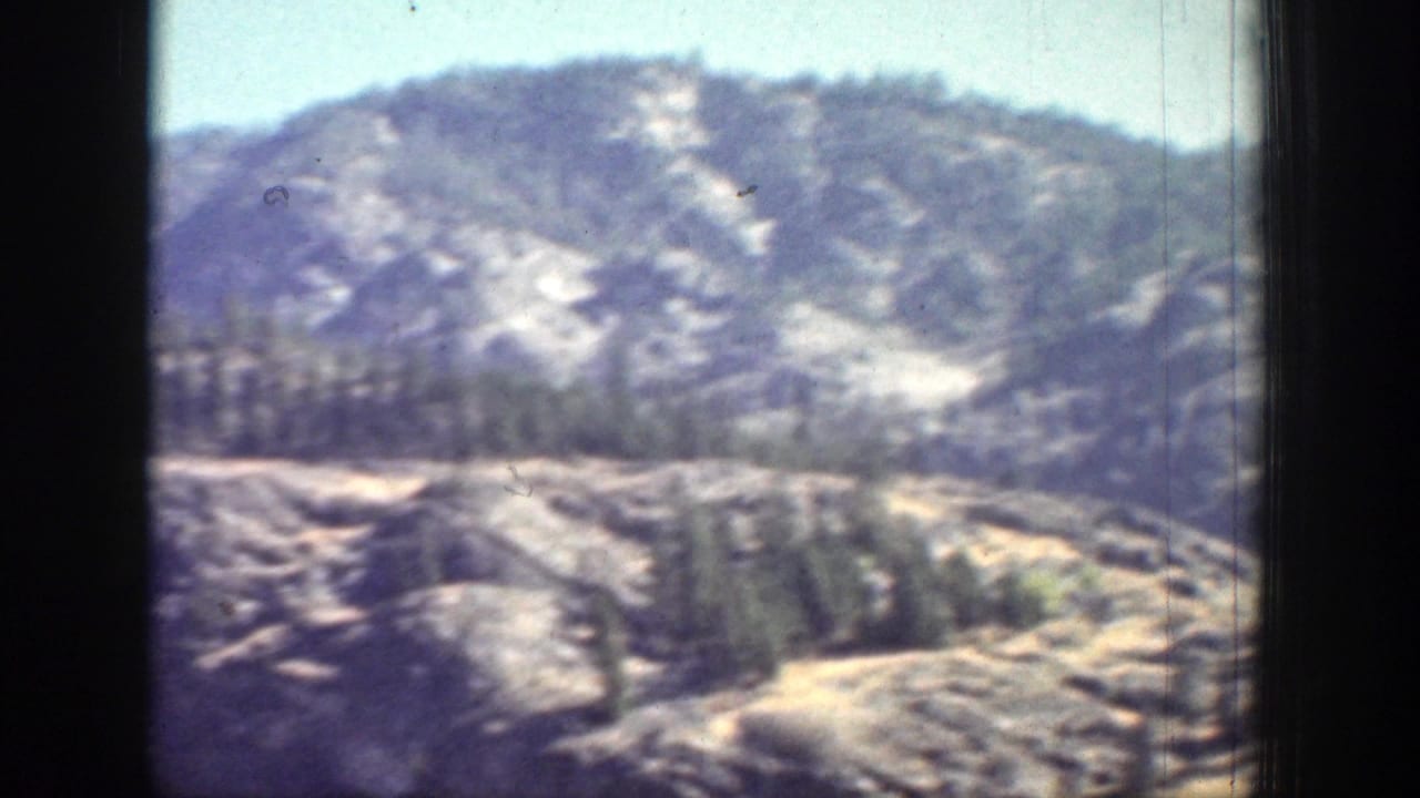 1939 Chelan, Washington frame with a distant rocky hillside, evergreen patches, and a pale winding path or open slope.