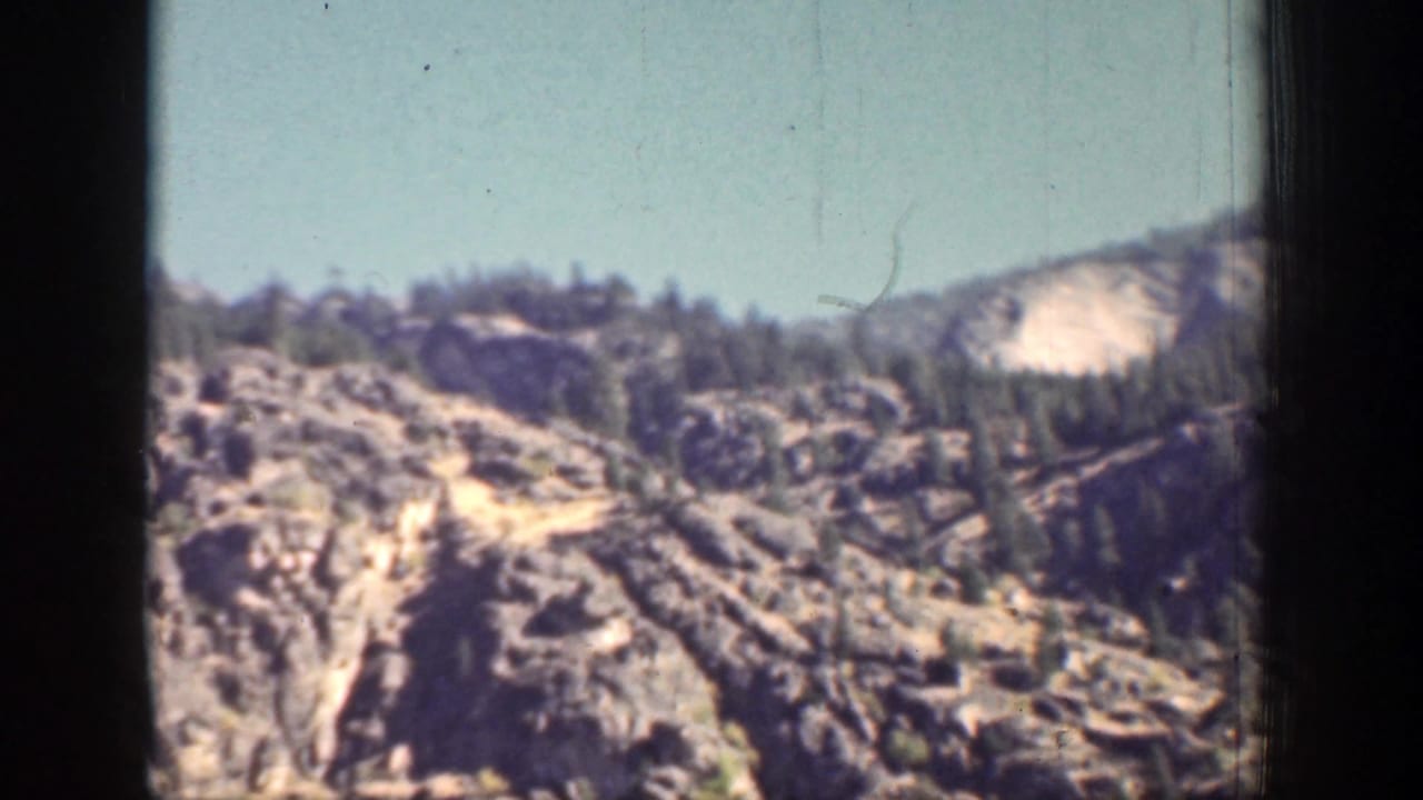 1939 Chelan, Washington frame with a rugged rocky ridge, scattered evergreen trees, and open blue sky.