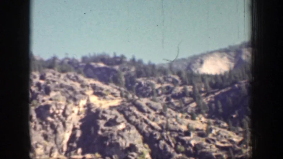 1939 Chelan, Washington frame with a rugged rocky ridge, scattered evergreen trees, and open blue sky.