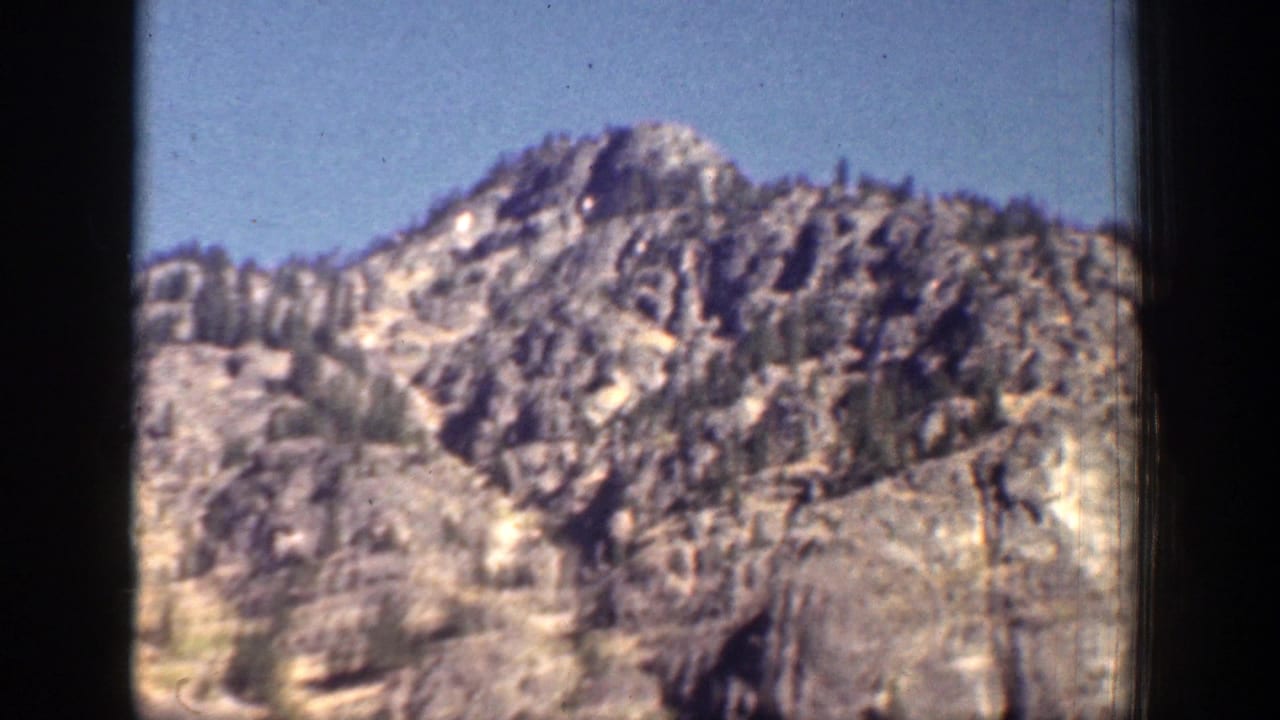 1939 Chelan, Washington home-movie frame showing a jagged rock outcrop and evergreen trees along the slope.