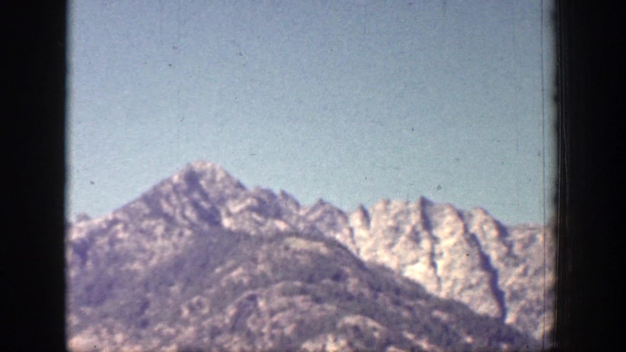 A rugged mountain ridge near Chelan, Washington appears under blue sky in faded 8mm color, framed by dark gate edges.
