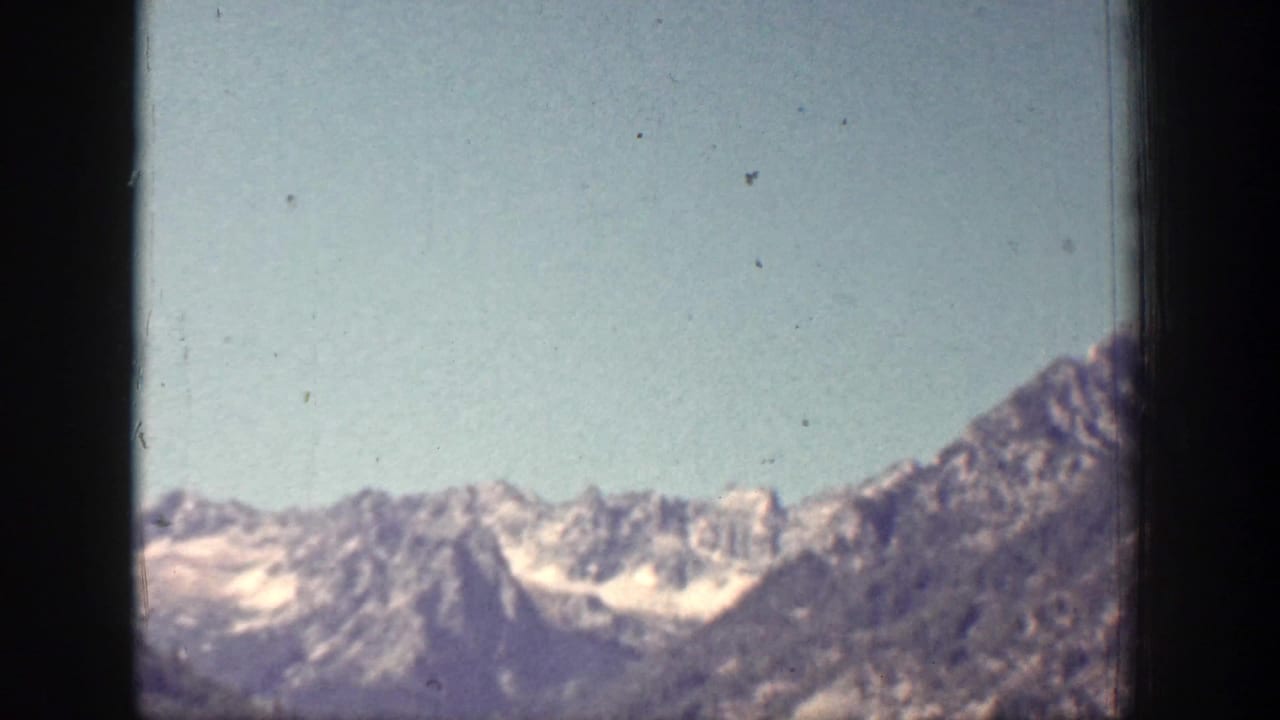 A wide 1939 home-movie view shows snow-streaked mountain peaks in the Chelan area beneath a clear blue sky.
