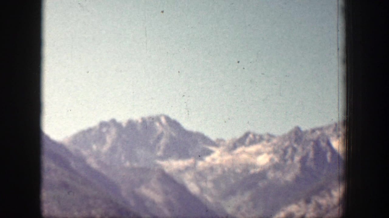 Distant Chelan-area mountains with snow patches sit under a pale sky, recorded with soft focus and visible 8mm film texture.