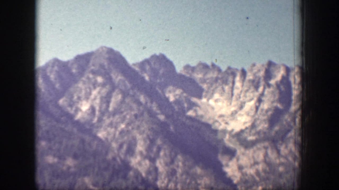 1939 Chelan, Washington frame with distant mountain peaks, rocky faces, and a hazy blue sky seen through 8mm film borders.