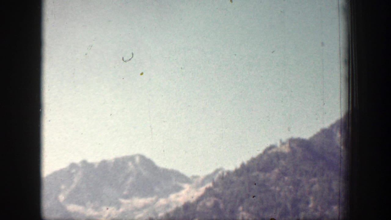 1939 Chelan, Washington home-movie frame showing a hazy wide view of mountain ridges and a darker foreground slope below open sky.