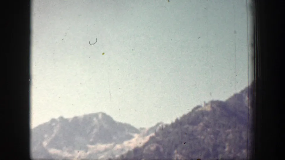 1939 Chelan, Washington home-movie frame showing a hazy wide view of mountain ridges and a darker foreground slope below open sky.