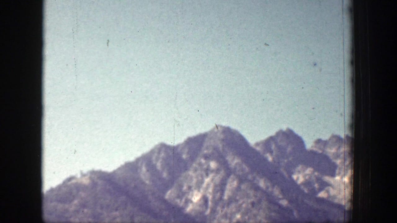 1939 Chelan, Washington frame showing mountain peaks, rocky ridgelines, and light haze within the borders of the 8mm film image.