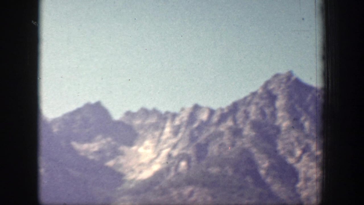 Chelan-area mountain peaks appear in a soft 1939 8mm frame, with rocky ridges, haze, and visible film gate edges.