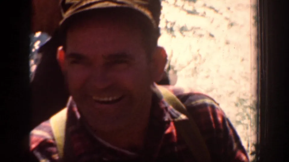 A smiling adult hiker appears briefly in the 1939 Chelan, Washington home movie, wearing a cap and plaid shirt near bright rock.