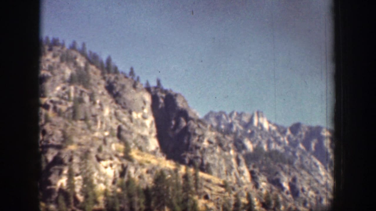 1939 Chelan, Washington frame showing rugged mountain rock faces, scattered trees, and clear blue sky.