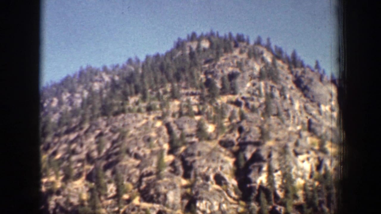 1939 8mm home-movie frame from Chelan, Washington showing a rocky, tree-lined mountain slope below a clear sky.