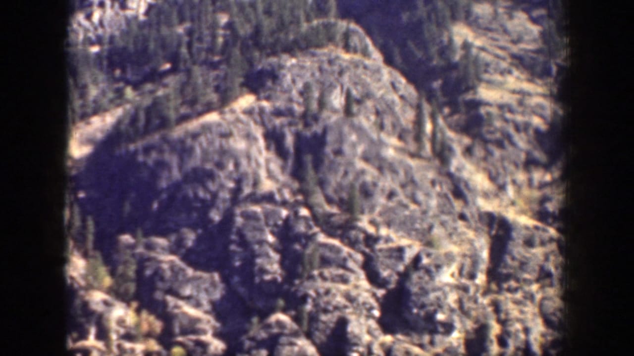 1939 Chelan, Washington frame with a closer view of rugged rock formations and sparse trees on a steep mountain slope.