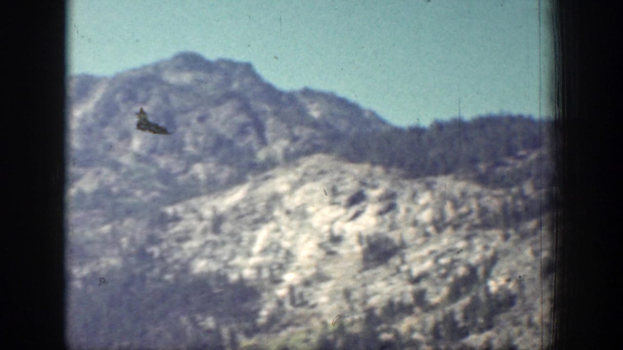 Vintage 8mm frame of a bright rocky Chelan mountain ridge with sparse trees and visible film wear.