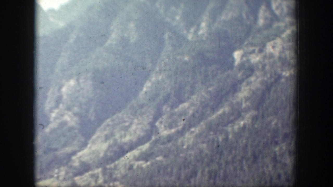Soft, hazy 1939 Chelan mountain view showing layered rocky slopes and dark evergreen forest below.