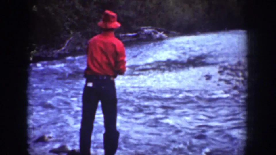1939 Chelan, Washington 8mm frame of a lone angler in red standing near rapid river water.
