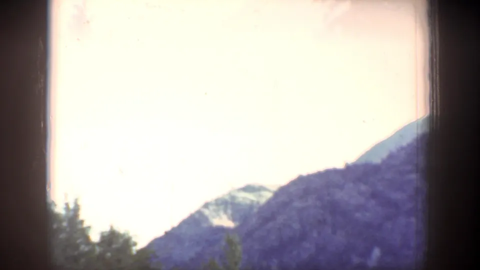 1939 Chelan, Washington frame with forested mountain slopes and a washed bright sky in faded color 8mm film.