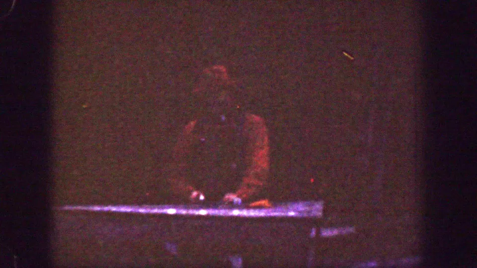 A heavily underexposed 8mm frame shows the man faintly at the riverside, with the waterline and red clothing still visible.