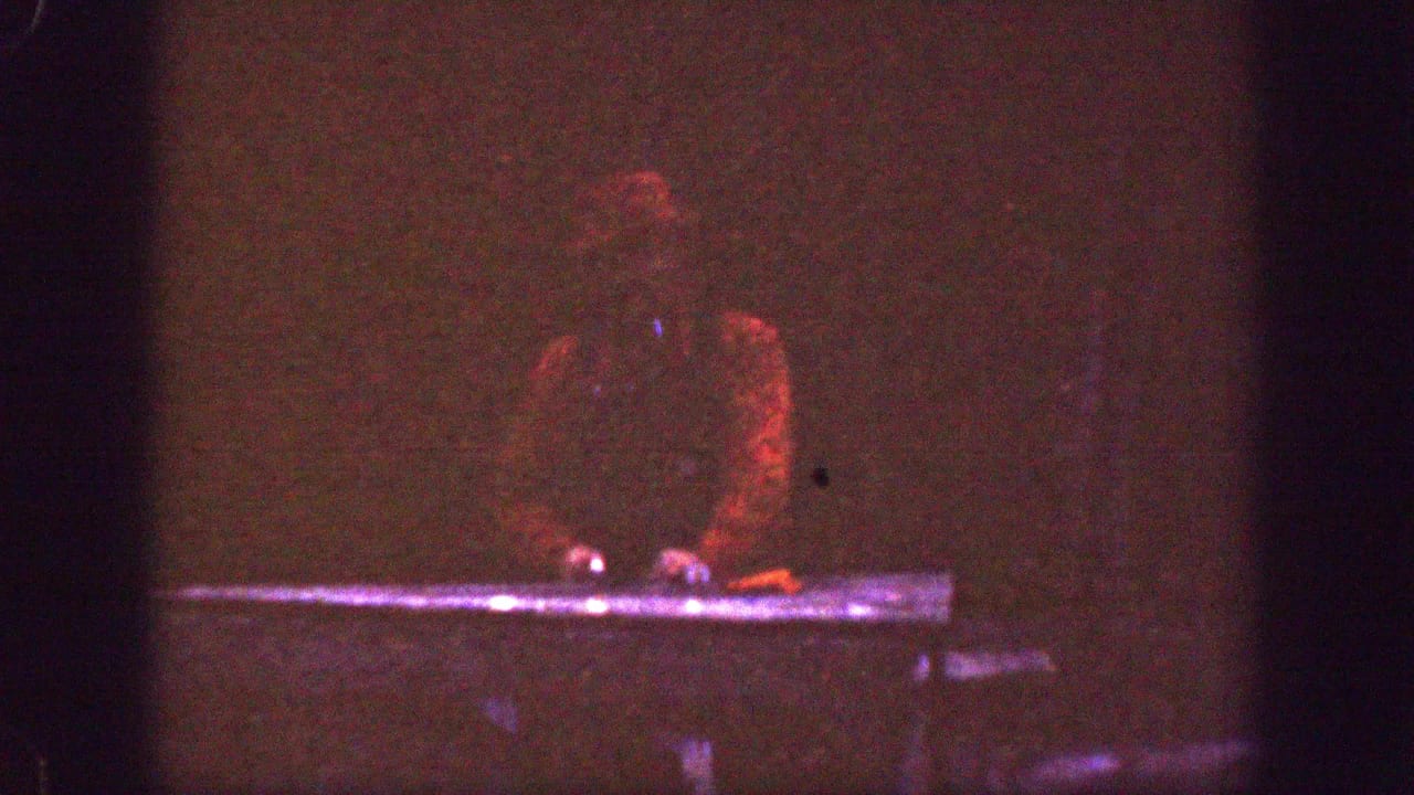 In 1939 Chelan home-movie footage, a man in a red cap works at a table in a very dark interior or shaded setting.