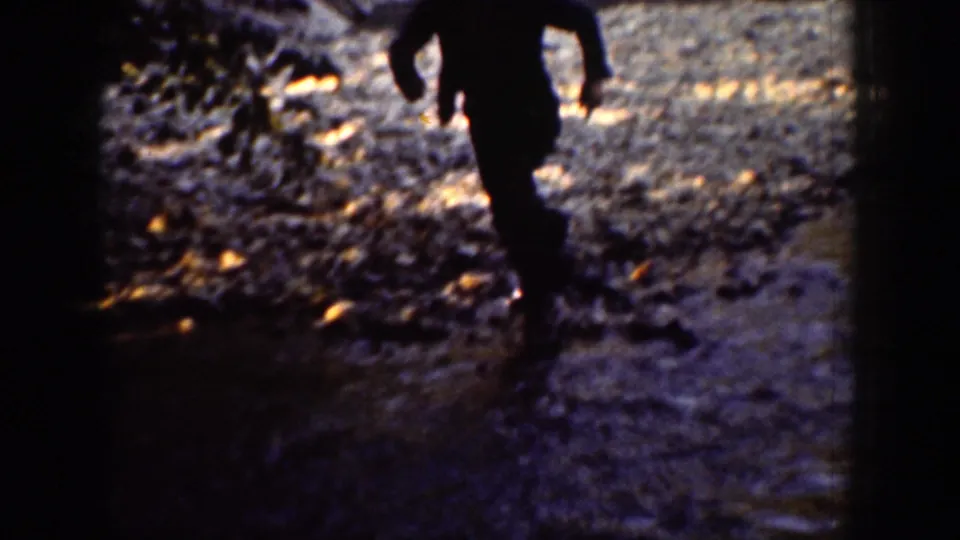 A shadowed figure moves close to the camera across the rocky river edge in the 1939 Chelan home-movie footage.