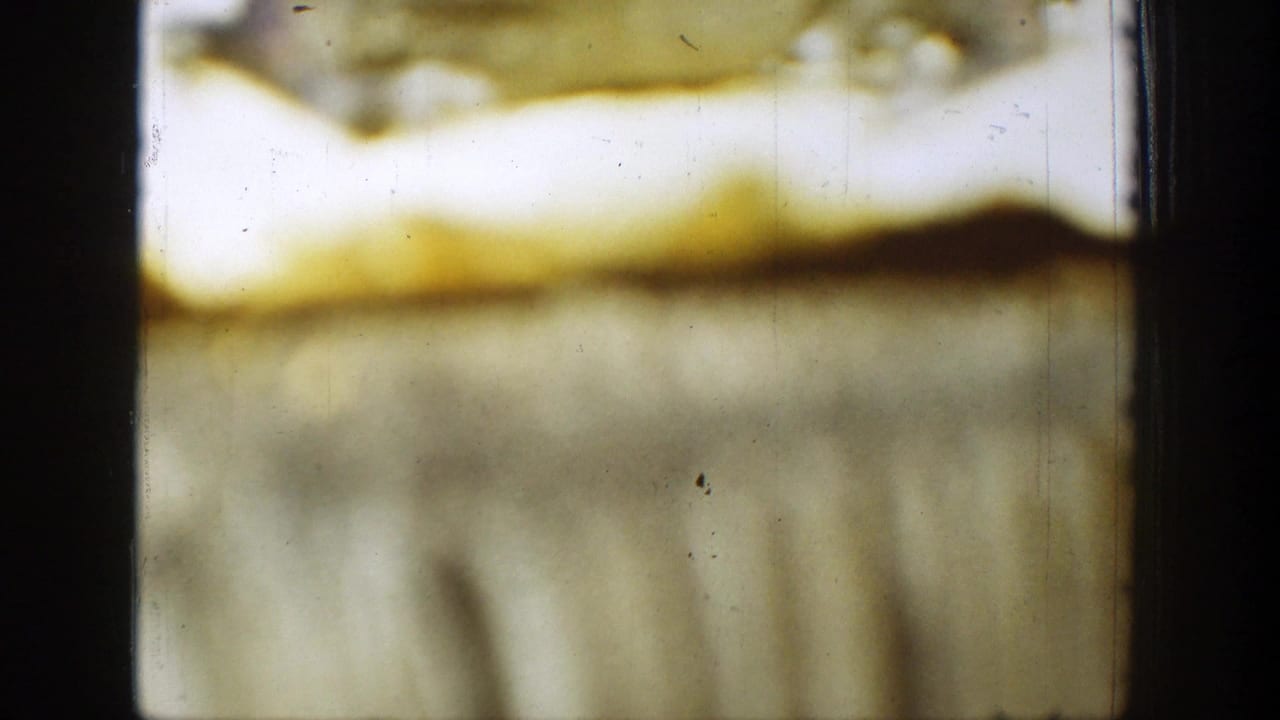 Soft yellowed 8mm frame texture with dark vertical borders and scratches.