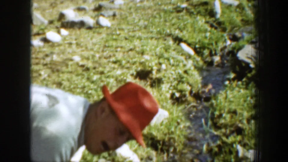 The final frame shows the red-hatted man crouched near a narrow stream with grass, stones, and bright outdoor light around him.