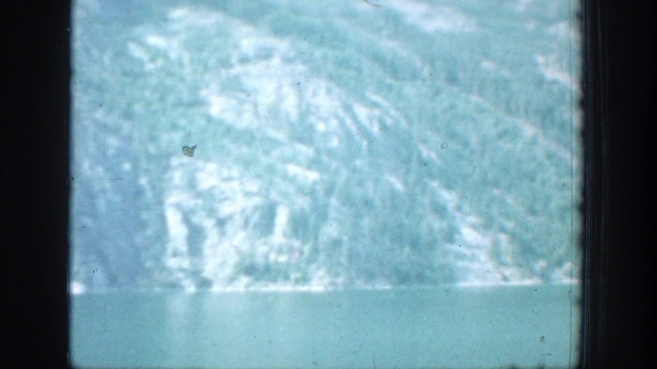 Blue-green lake and snowy mountain slope seen through dark window framing.