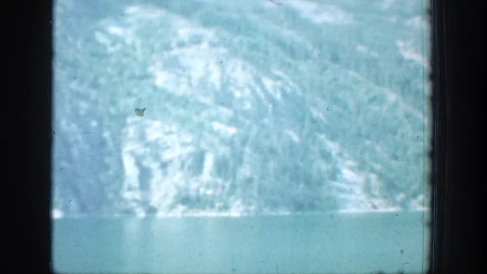 1939 Chelan, Washington home-movie frame showing lake water and snow-dusted mountains through a dark window edge.