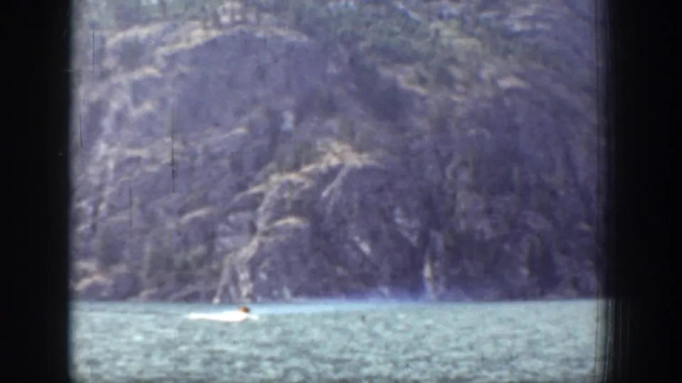 1939 Chelan footage frame with a small boat low in the composition, mountain shoreline, and visible 8mm scan marks.