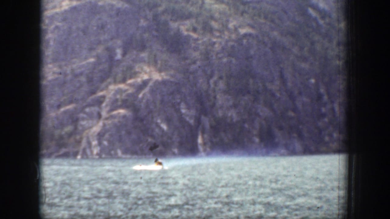 A distant motorboat moves across a lake in Chelan, Washington, with forested mountains beyond and dark window framing in the foreground.