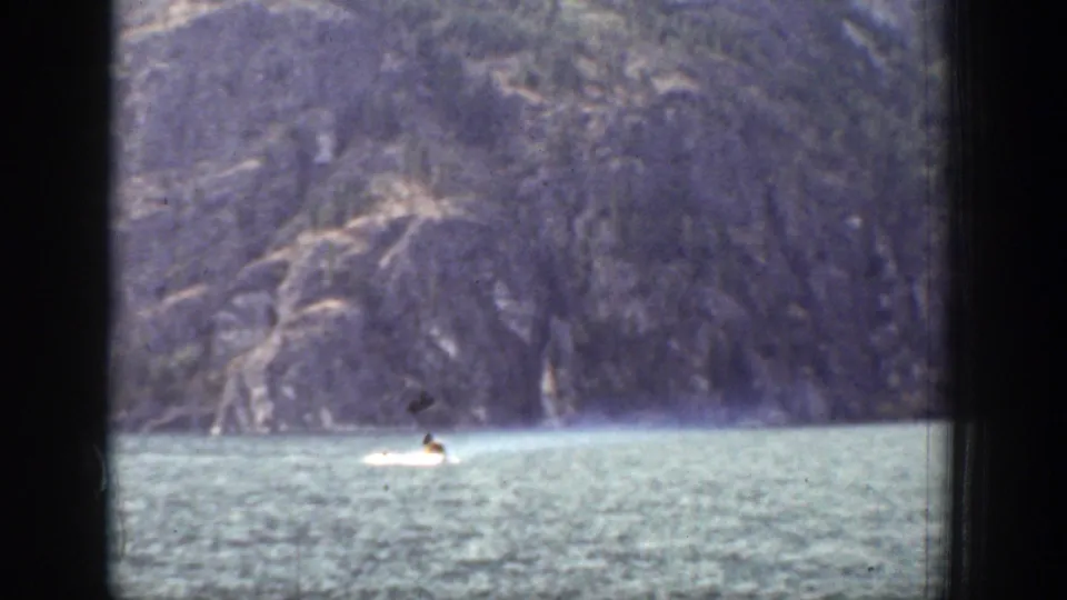 A distant motorboat moves across a lake in Chelan, Washington, with forested mountains beyond and dark window framing in the foreground.