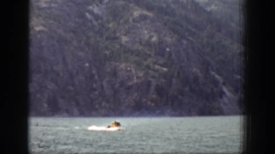 The motorboat continues across the Chelan lake scene, framed by dark vertical foreground edges and a steep wooded shoreline.