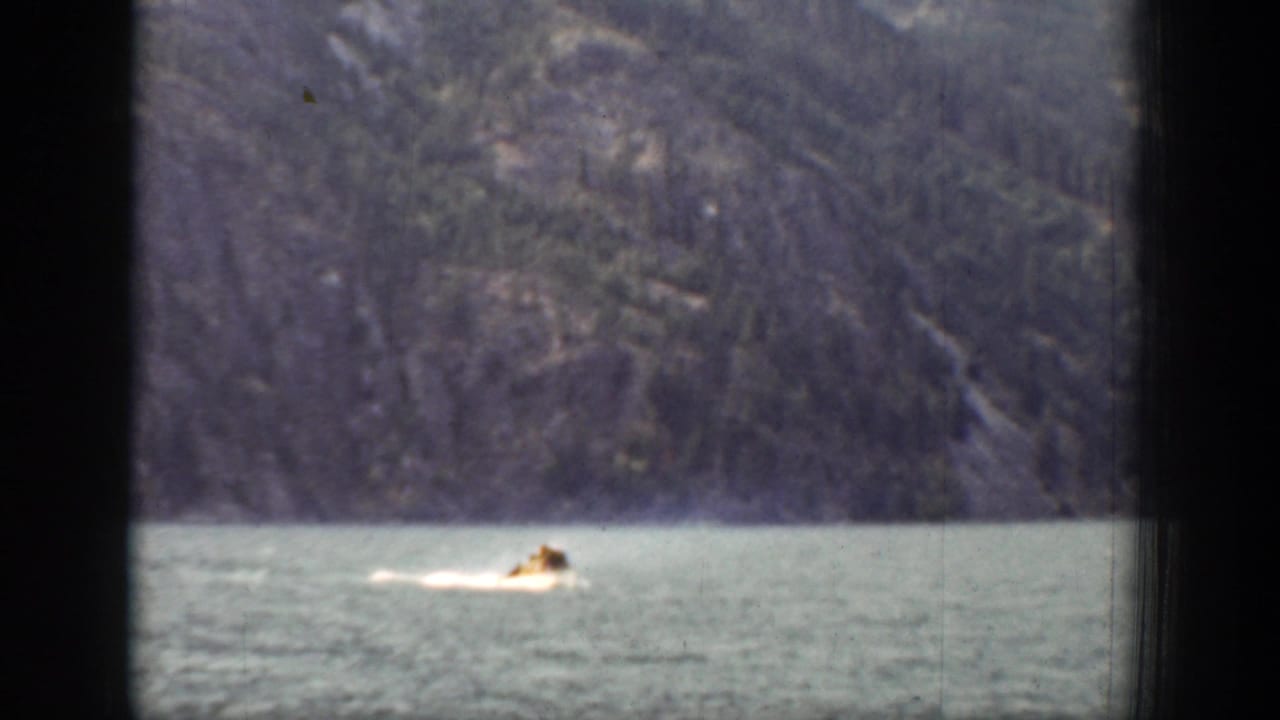 A small boat appears low in the frame on the Chelan lake, with blue-green water, wooded mountains, and heavy dark window bars visible.