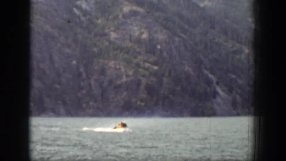 A small boat appears low in the frame on the Chelan lake, with blue-green water, wooded mountains, and heavy dark window bars visible.