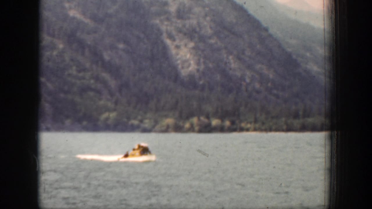A small white motorboat moves across Lake Chelan, Washington, with forested mountains in the background in 1939 8mm footage.