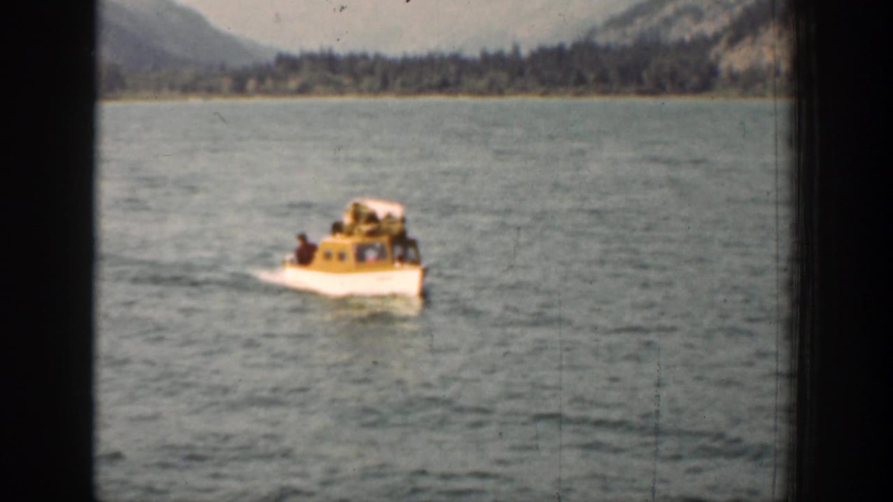 Small yellow-and-white boat crosses lake water with mountains and shoreline behind it.