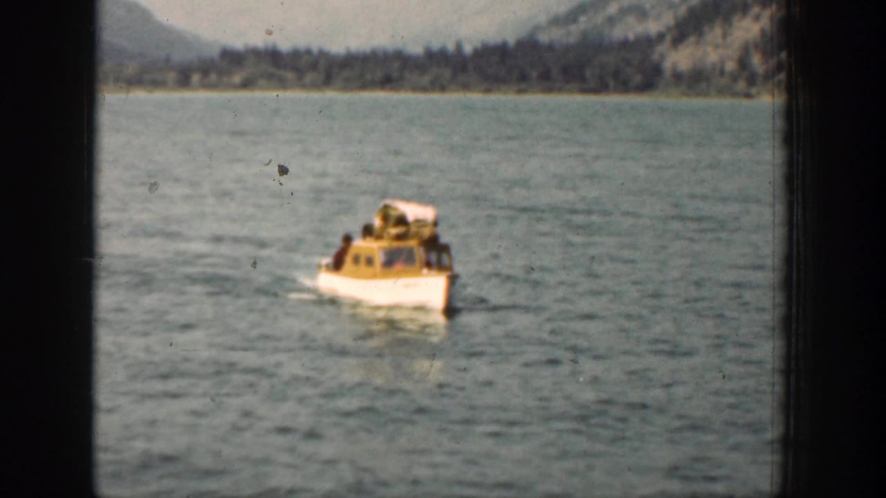 Passenger boat continues across the lake, leaving a wake near a wooded mountain shoreline.