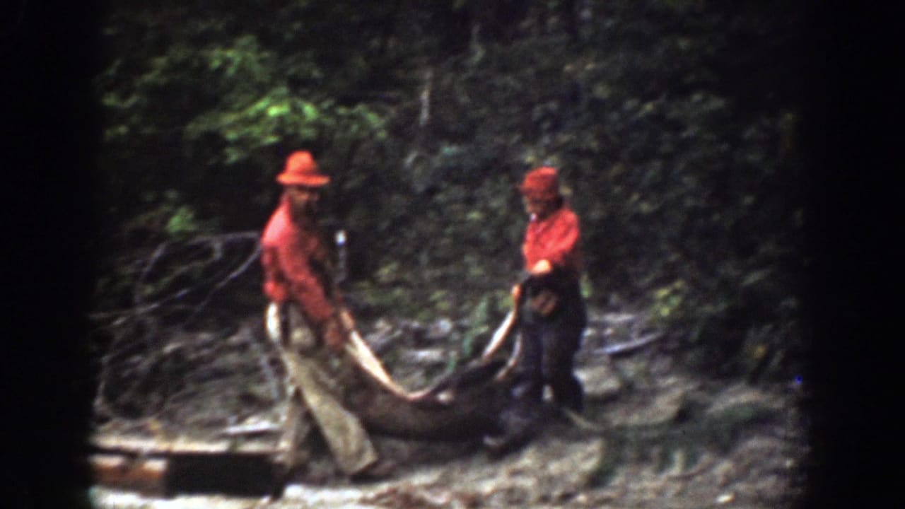 Two men in red clothing hold a large carcass or hide near a wooden sled in 1939 Chelan, Washington home-movie footage.